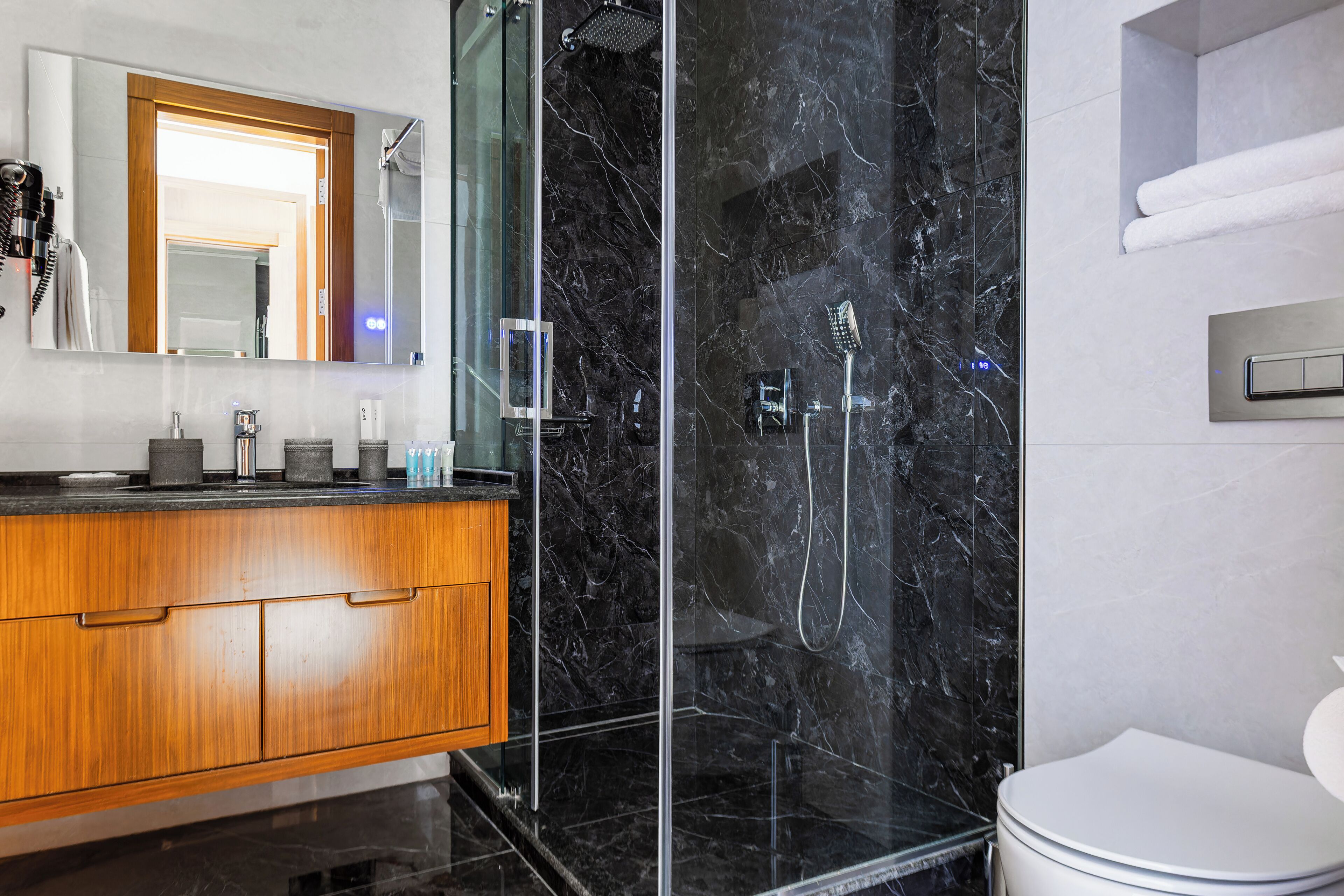 Une salle de bain moderne avec une douche à parois de verre, un meuble-lavabo en bois et des toilettes blanches.