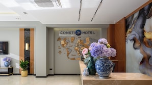 A hotel reception area with a marble floor, a reception desk with vases of flowers, a world map on the wall, and a sign reading "Consti Hotel". - Consti Hotel Tashkent (Tashkent)