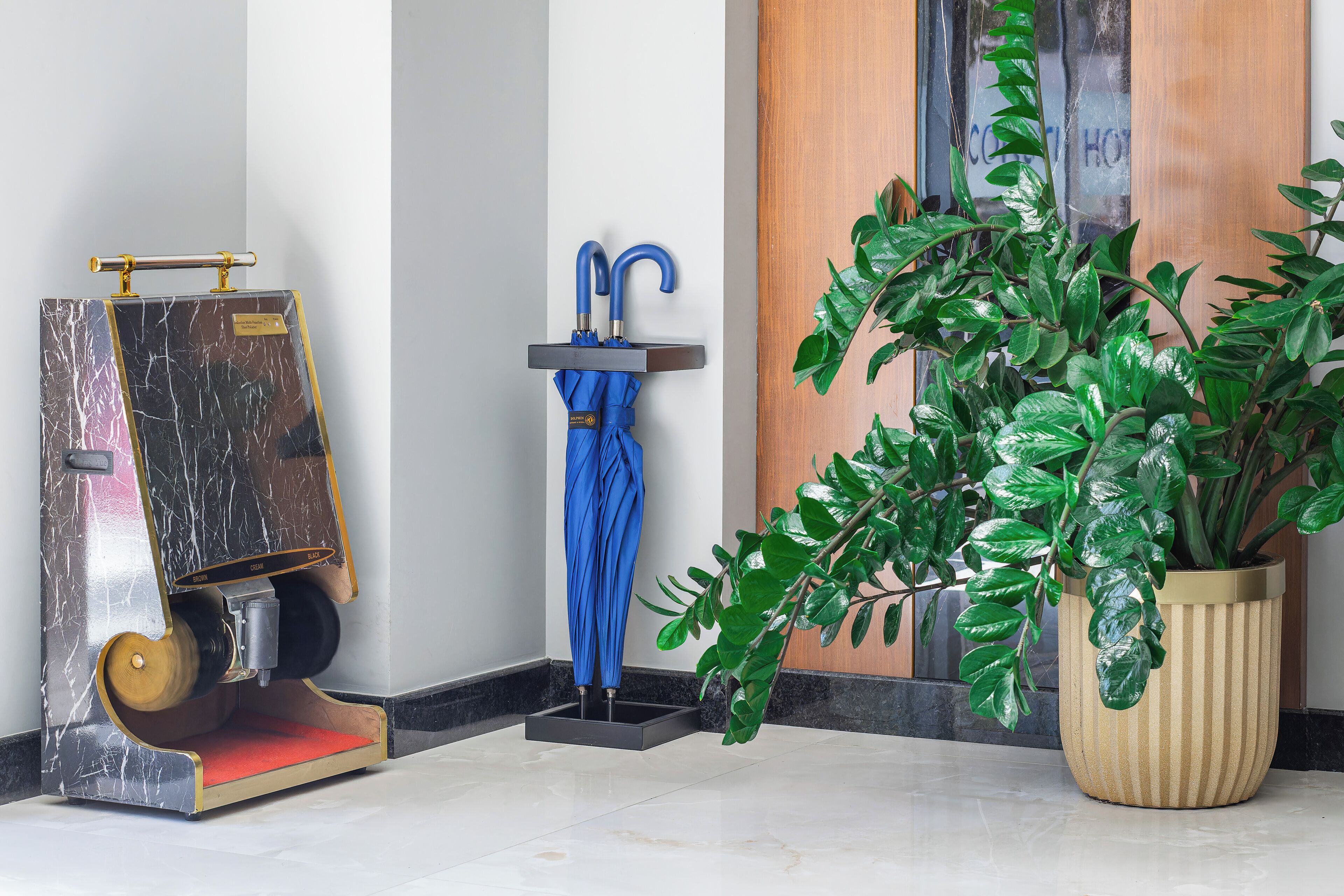 A marble floor, a blue umbrella, a plant in a striped pot, and a wooden door.
