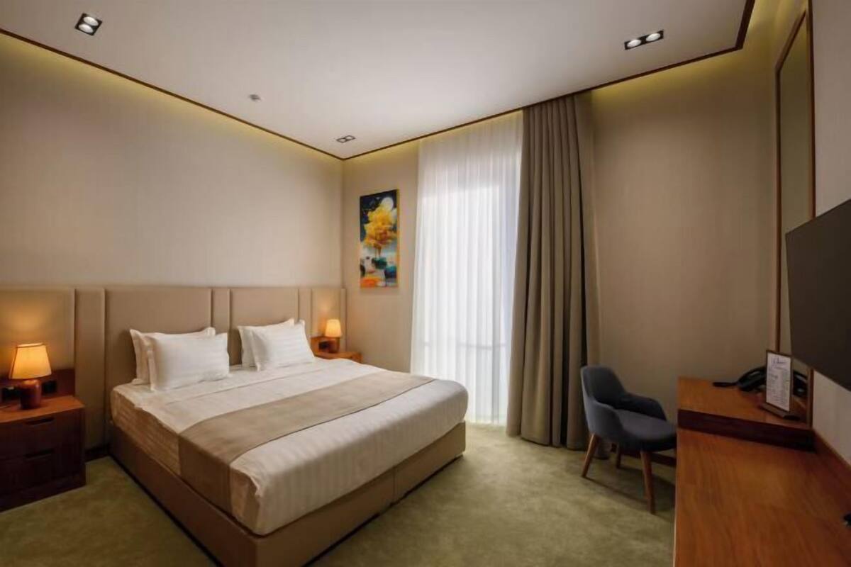 A hotel room with a large bed, bedside lamps, a desk, and a television.