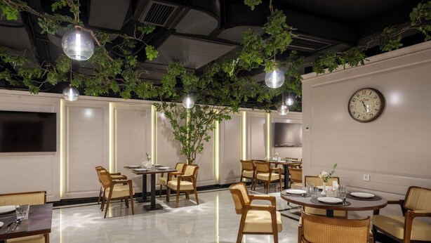 A restaurant with round tables, chairs, hanging plants, pendant lights, and a wall clock. - Consti Hotel Tashkent (Tashkent)