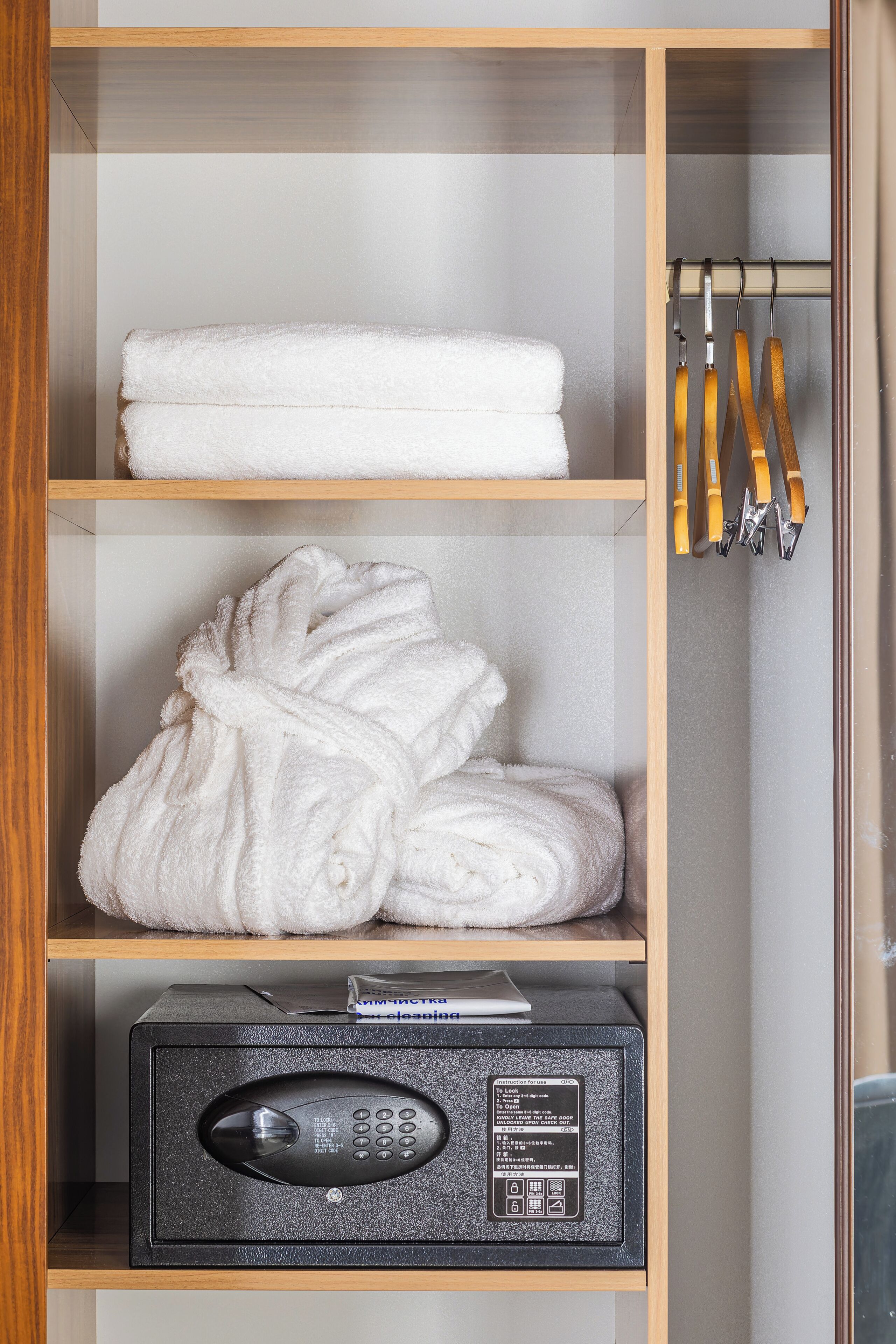 A hotel room with a wooden shelf holding rolled towels and a black electronic device, possibly a safe or control panel.