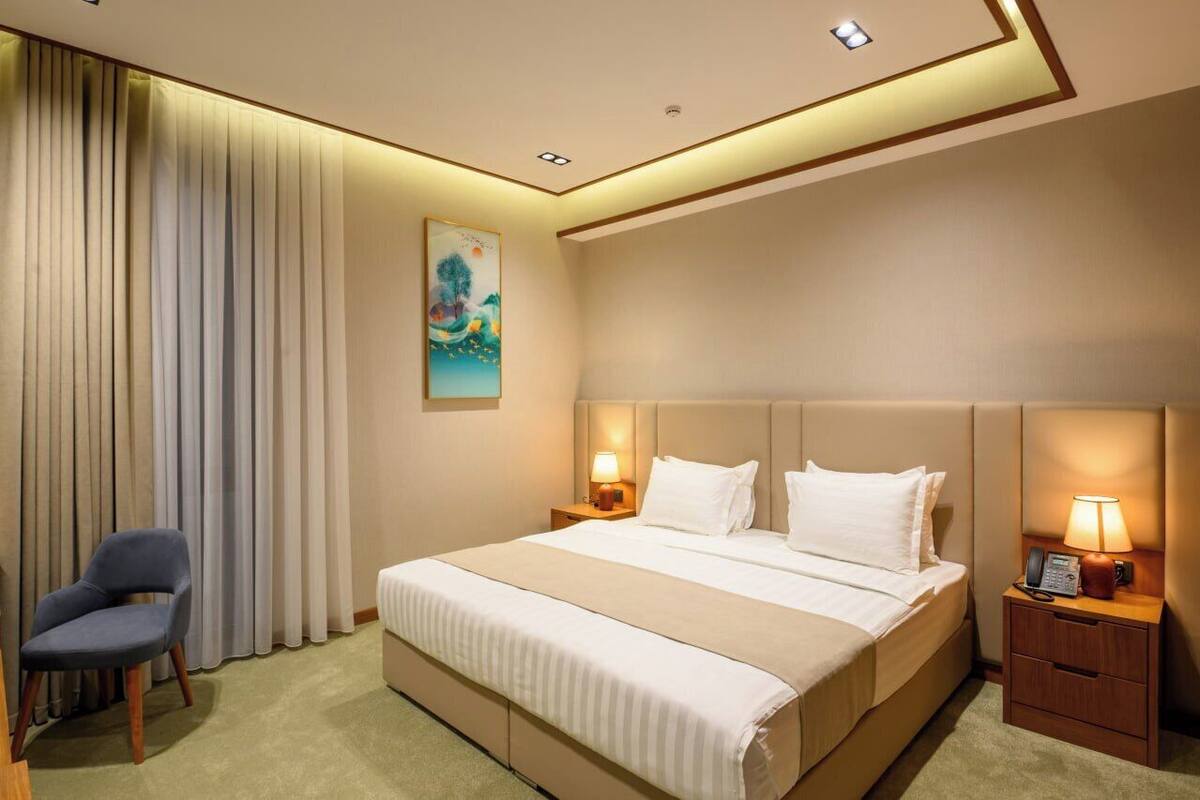 A hotel room with a large bed, two bedside tables with lamps, a chair, and a painting on the wall.