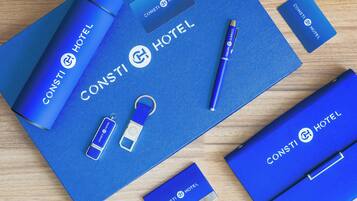 Un juego de artículos de papelería de hotel que incluye un bolígrafo, un llavero, una tarjeta de presentación y una libreta, todos con la marca 'CONSTI HOTEL'.