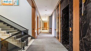 Een hotelgang met tapijtvloer, een trap met glazen leuning en een wand van zwart marmer.