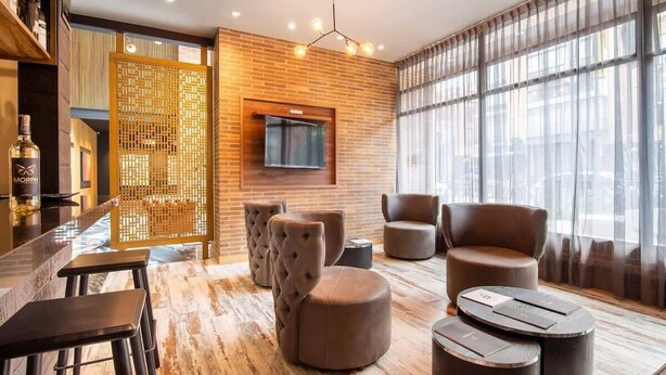 Ein stilvoller Lounge-Bereich mit Ledersitzmöbeln, einer Bar und einem großen Fenster mit Vorhängen.