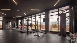 Ein Fitnessstudio mit verschiedenen Trainingsgeräten, großen Fenstern und Blick ins Freie.