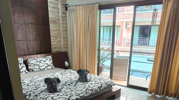 A bedroom with a bed, a chair, and a view of an outdoor area. - Kata Happy Place (Karon)