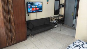 A living room with a sofa, a TV mounted on the wall, a clock, and a door leading to another room. - Kata Happy Place (Karon)