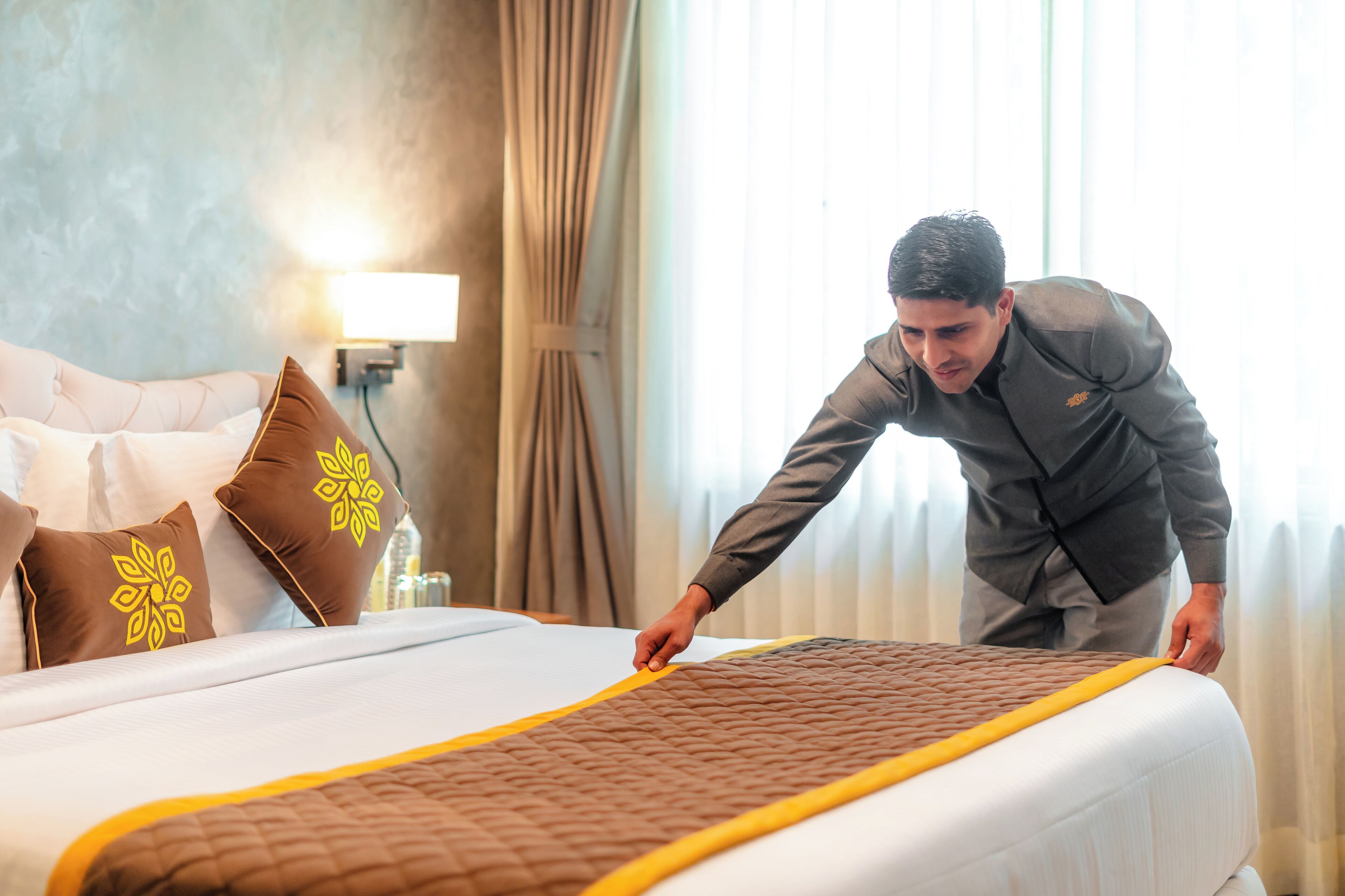 A hotel room with a neatly made bed, a lamp, and curtains.