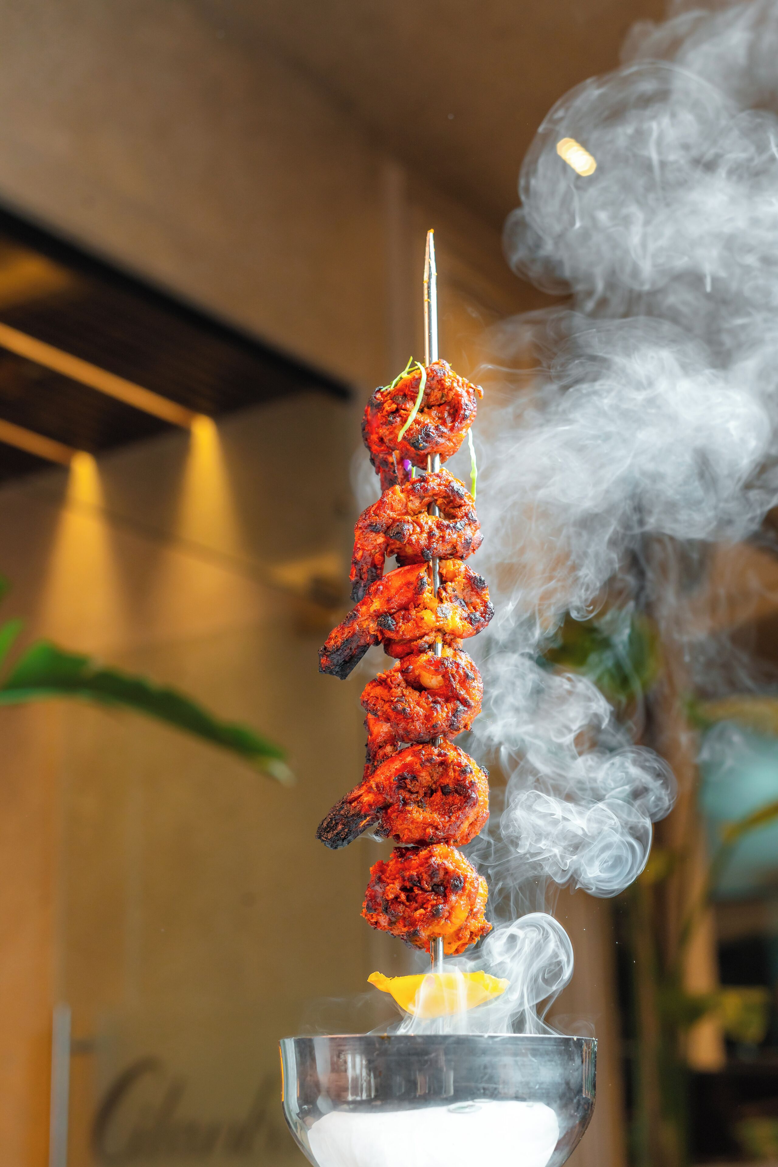 Une brochette de viande grillée, de laquelle s’échappe de la fumée, est posée sur un verre contenant une tranche de citron.