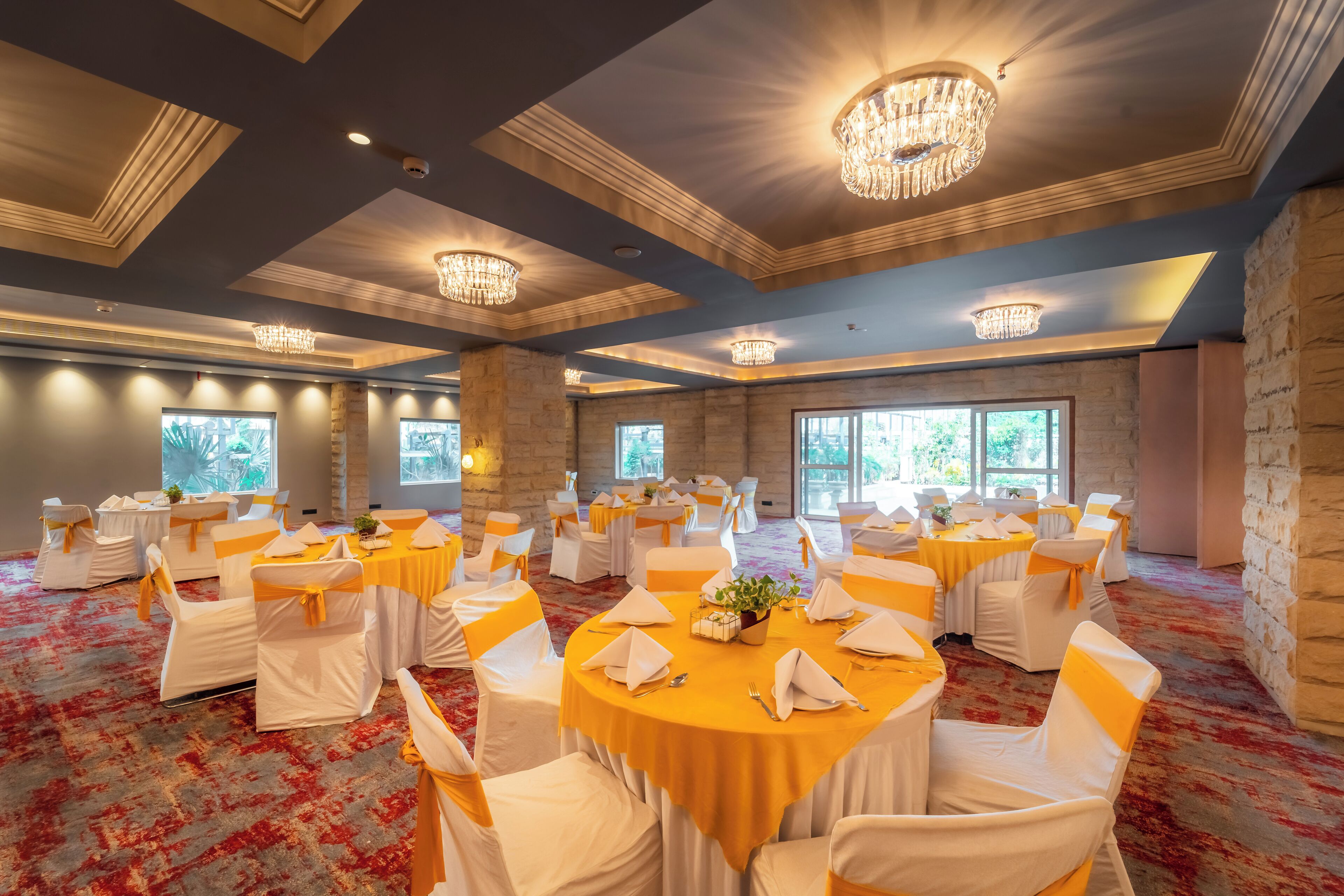 A banquet hall with round tables, white chairs, and chandeliers.