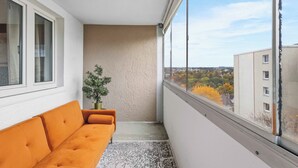 A balcony with a sofa, a potted plant, and a view of buildings and trees. - City Apartment | View & WIFI (Kempten (Allgäu))