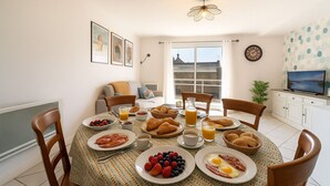 A dining area with breakfast items, a television, and a view of the city. - Comfortable T3, walking distance to the beach - Secure garage (Dinard)