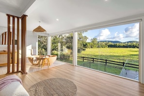 A spacious room with a large sliding glass door leading to a balcony, a wooden floor, a round rug, and a modern bathroom with a bathtub.
