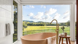 A modern bathroom with a freestanding bathtub, a wooden stool, and a view of a green landscape through a glass door. - Paddock View Ranch in the Sunny Coast Countryside (Belli Park)