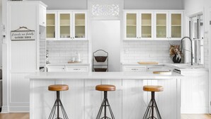 A kitchen with white cabinetry, a central island with stools, a ceiling fan, and a 'friends and family gather here' sign. - Paddock View Ranch in the Sunny Coast Countryside (Belli Park)