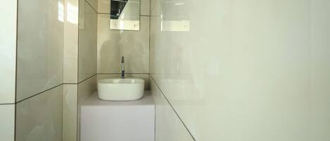 Un baño moderno con un lavamanos blanco, un espejo y una lámpara.
