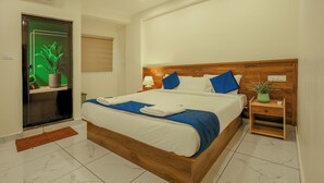 A neatly made bed with a wooden headboard, a bedside table with a lamp, and a potted plant. - MOONIC DAYS (Kanayannur)