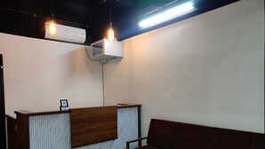 A reception area with a wooden reception desk, a brown sofa, and a hanging light fixture. - MOONIC DAYS (Kanayannur)