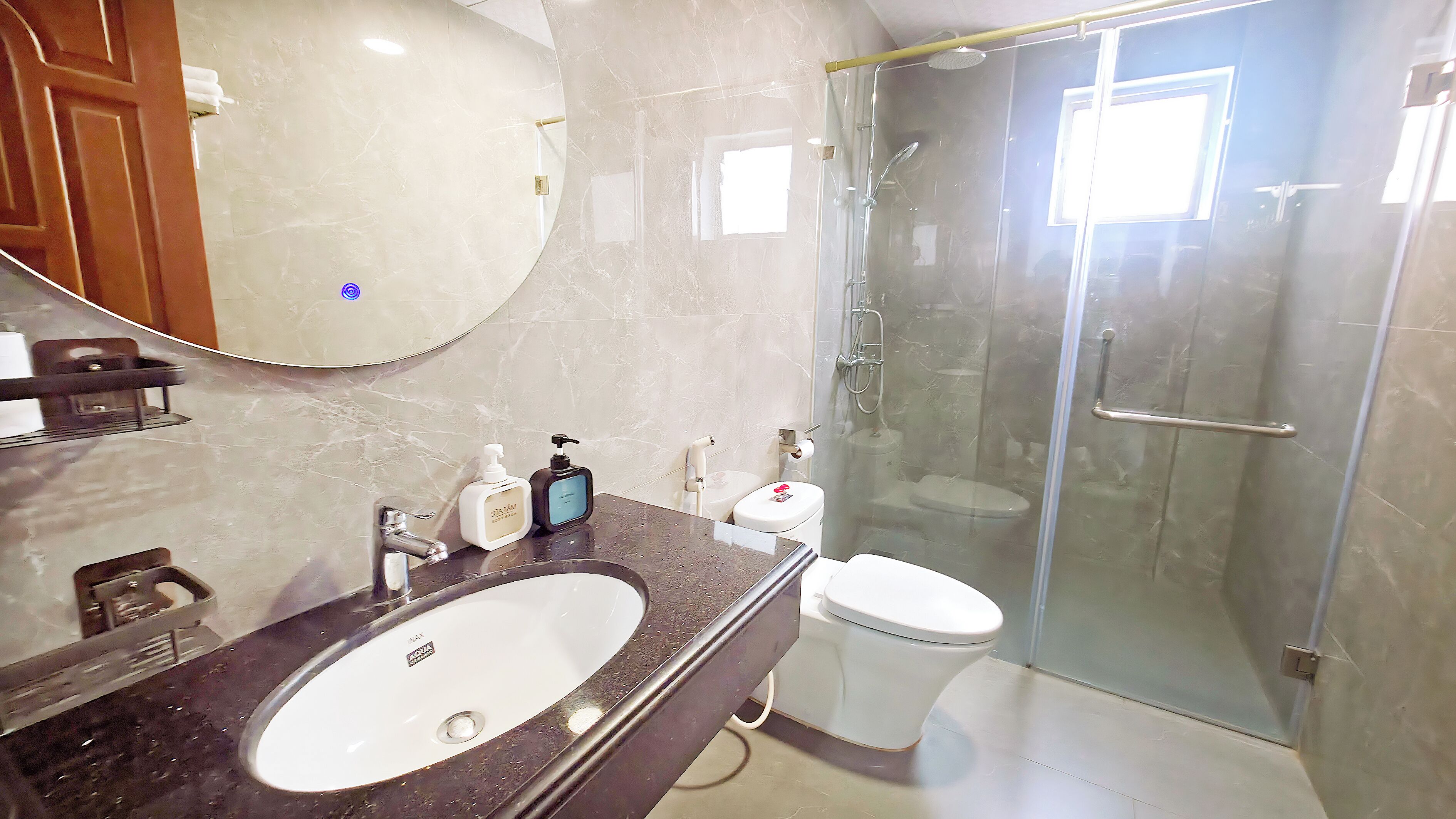 Un baño con lavamanos de mármol, inodoro, cabina de ducha de vidrio y un espejo grande.