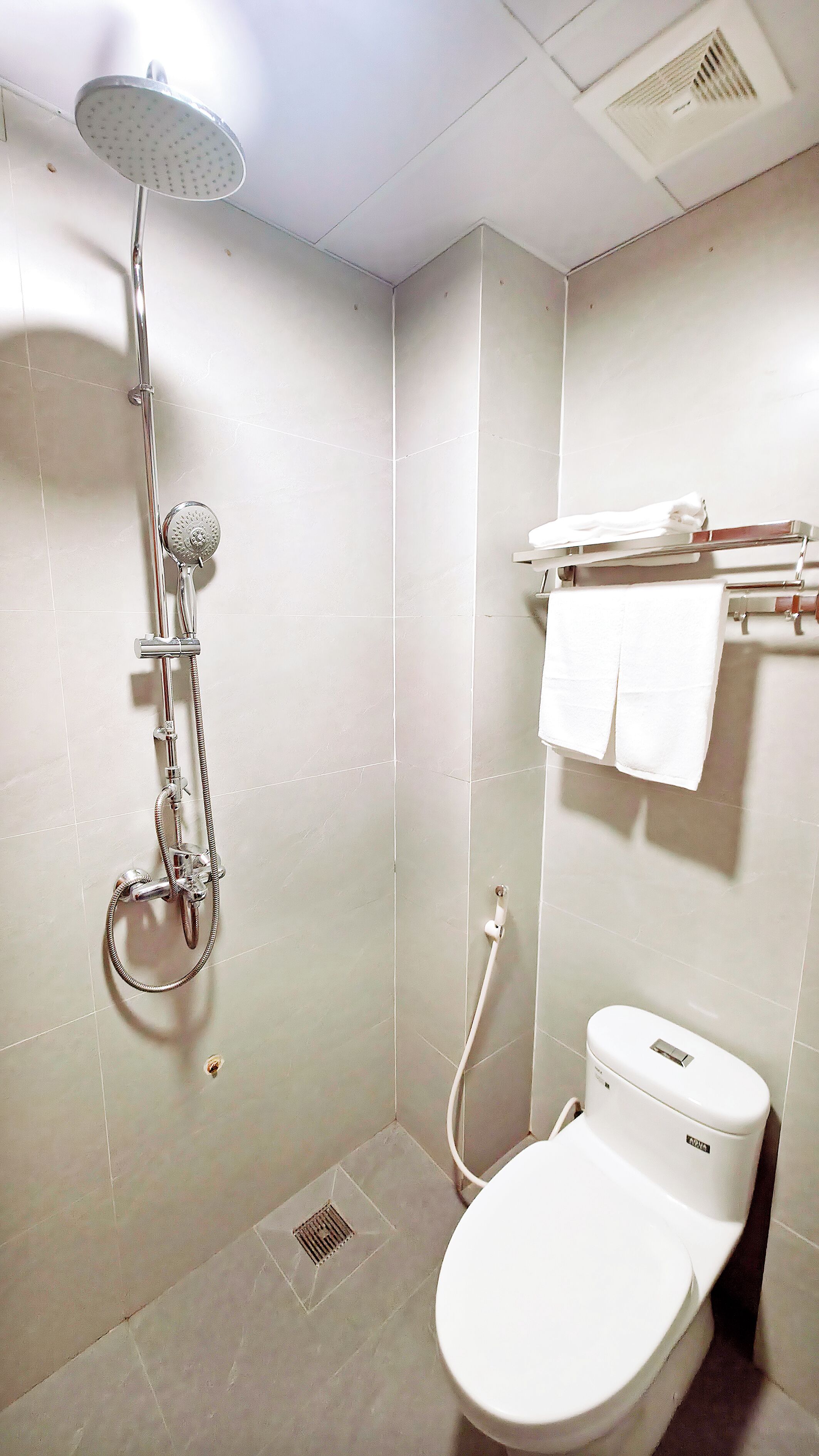 A small, tiled bathroom with a shower, toilet, and towel rack.