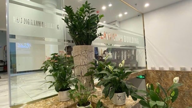 A modern interior with a marble reception desk, potted plants, and a glass wall displaying the name 'HIDIGELLAVAN BUILDING'. - Huong Linh Apartment (Hanoi)