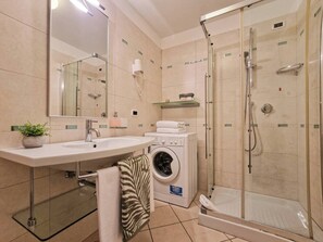 Ein modernes Badezimmer mit Waschbecken, Spiegel, Waschmaschine und einer Duschkabine.