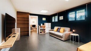 A modern living room with a sofa, a small table, and a TV mounted on a wooden panel. - Between the hills bordering Italy (Modern Flat) (Vacallo)