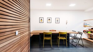 A dining area with a wooden table and chairs, framed artwork on the wall, and a shelf with books and items. - Between the hills bordering Italy (Modern Flat) (Vacallo)