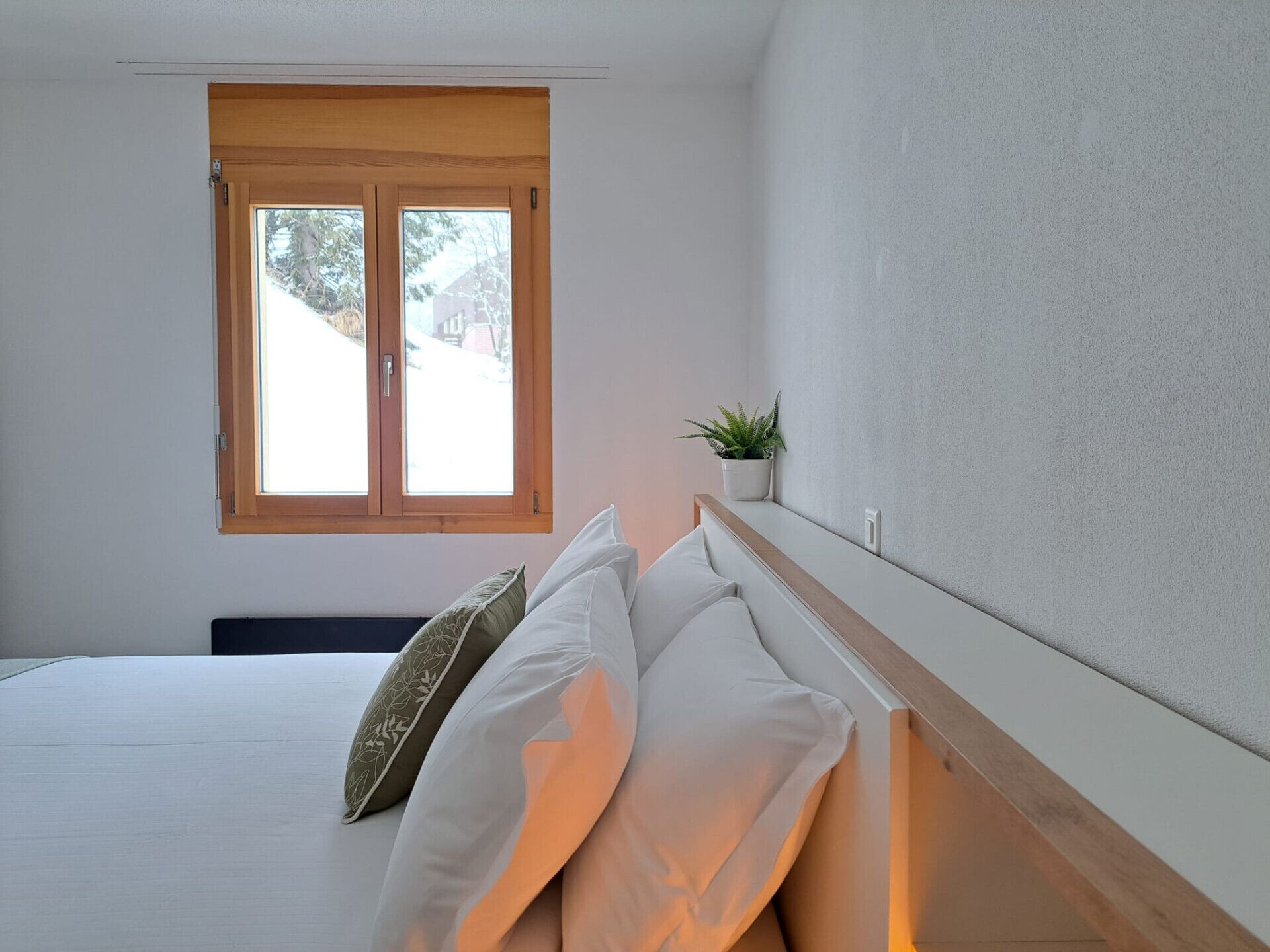 A bedroom with a bed, a window, and a small plant on the nightstand.