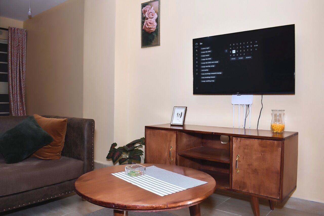 Una sala de estar con un sofá de cuero marrón, una mesa de centro de madera, un aparador de madera y un televisor de pantalla plana montado en la pared.