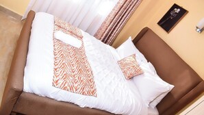 A neatly made bed with patterned pillows and a brown headboard in a room with beige walls and curtains.
