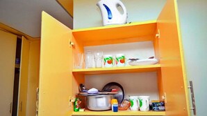 A kitchen with an open cabinet containing a kettle, glasses, a pot, and some mugs.