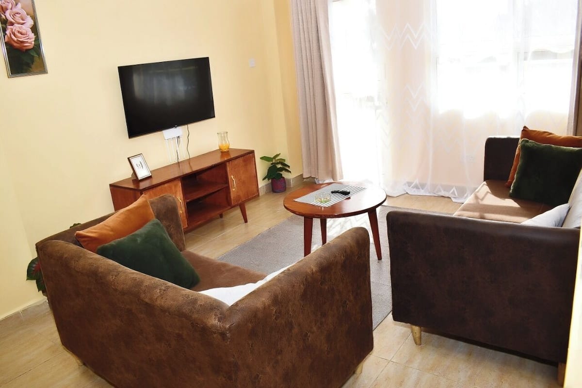A living room with a sofa, a smaller armchair, a coffee table, a TV, and a small cabinet.