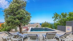 A poolside area with lounge chairs and a hot tub, surrounded by trees and buildings. - Villa Barbara (Klenovica)