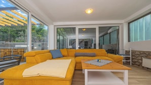 A modern living room with a yellow sofa, a wooden coffee table, and a view of a garden through large windows. - Villa Barbara (Klenovica)