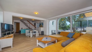 A modern living room with a large sofa, a dining area, and a staircase leading to another level. - Villa Barbara (Klenovica)