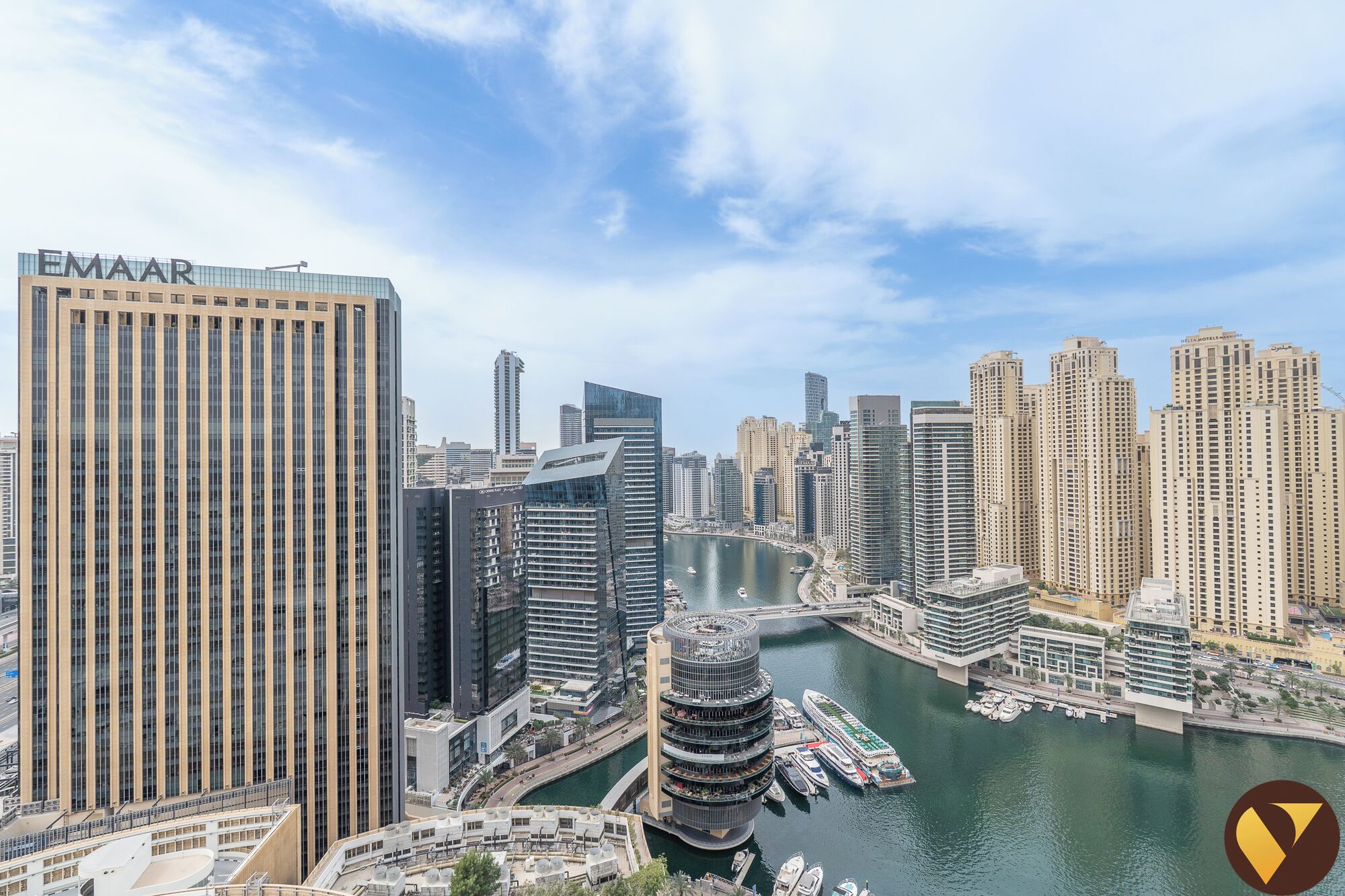 A high-rise building with the name 'EMAAR' on its facade, surrounded by other tall buildings and a marina with boats.