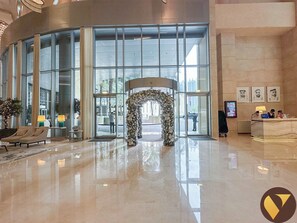 Eine geräumige Lobby mit Glastür, einer Rezeption und einer Sitzecke mit Sesseln.