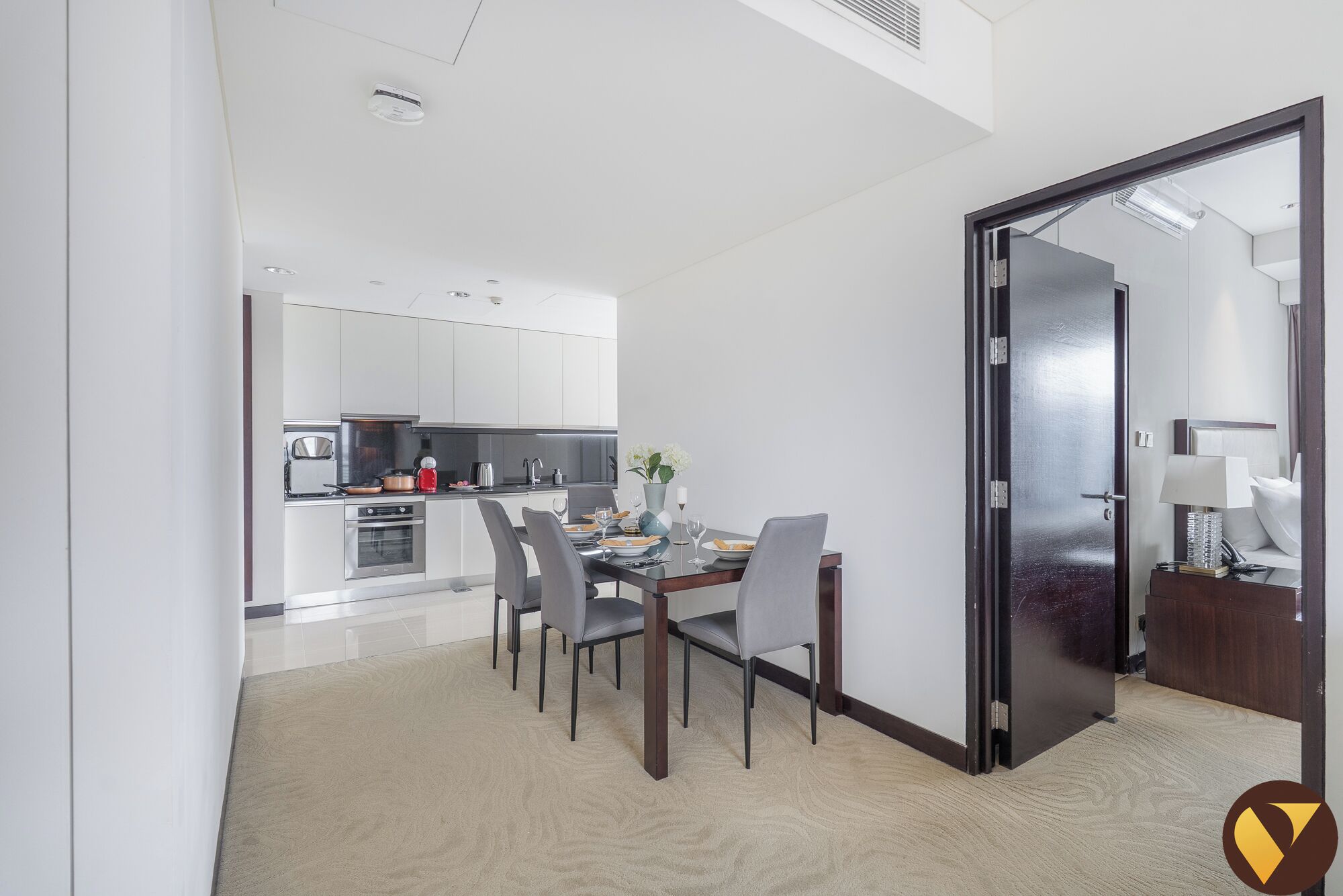 A modern kitchen with white cabinets, a dining area with a table set for four, and a sliding door leading to a bedroom.