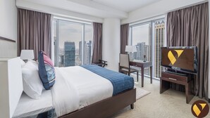 Ein Hotelzimmer mit einem großen Bett, einem Schreibtisch mit Stuhl, einem Fernseher und Blick auf die Stadt durch große Fenster.