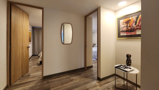 A hallway with wooden flooring, a mirror on the wall, and a table with a vase. - Cozy Loft Chpinero in Bogot (Bogotá)