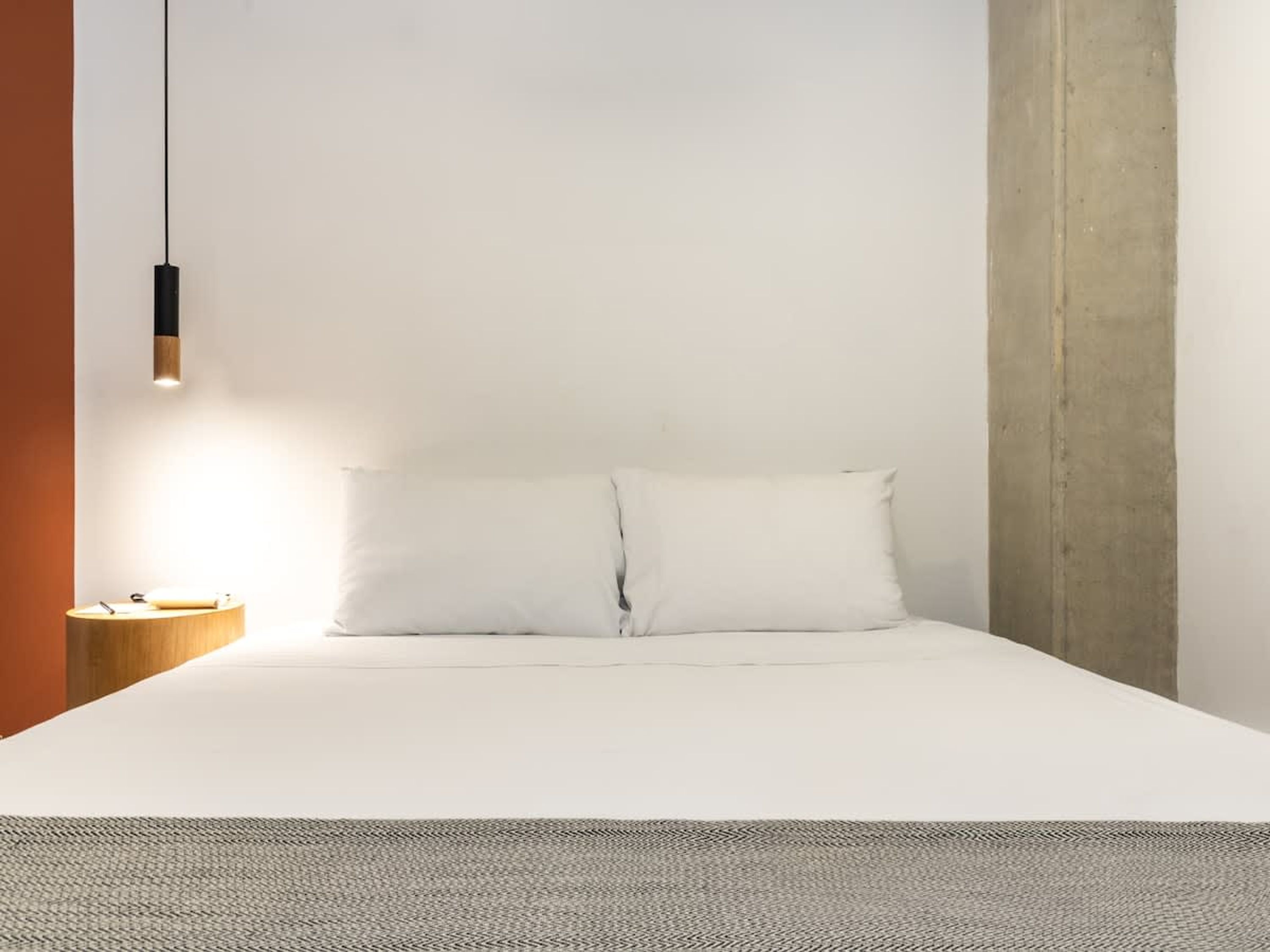 Une chambre à coucher au style minimaliste, avec un lit, une table de chevet et un luminaire suspendu.