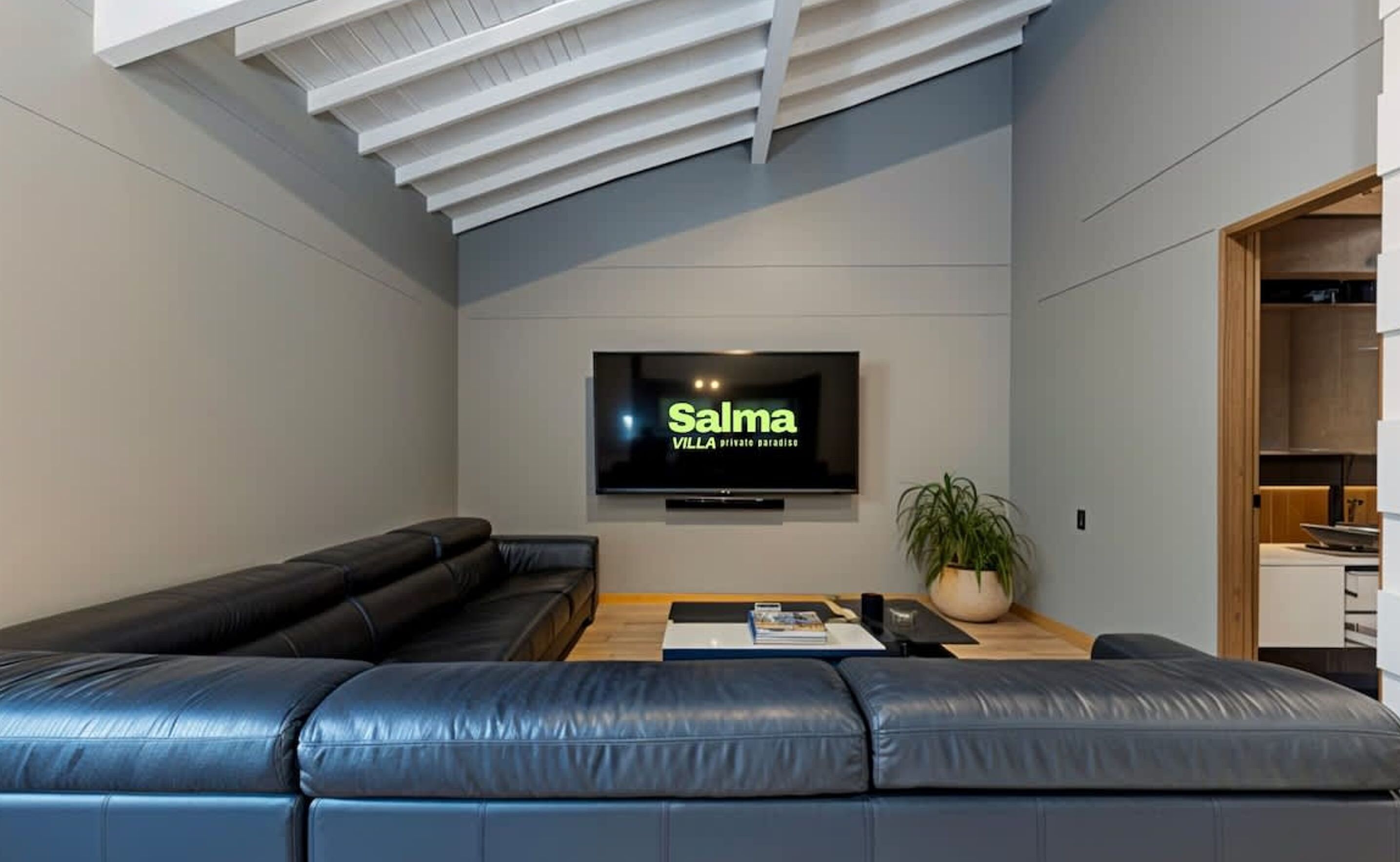 A modern living room with a black leather sofa, a flat-screen TV mounted on the wall, and a wooden coffee table.
