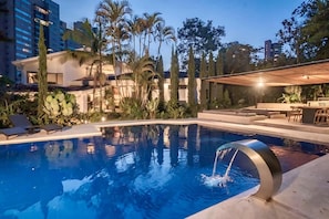 A swimming pool with a water feature, surrounded by palm trees and a covered seating area.