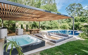 Area piscina esterna moderna con idromassaggio, zona relax coperta e tavolo da pranzo.