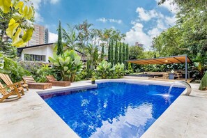 Una piscina con muelle de madera, rodeada de exuberante vegetación y un área de estar cubierta.