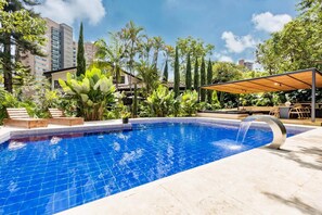 Una piscina con azulejos azules cristalinos, rodeada de exuberante follaje y una pérgola de madera.