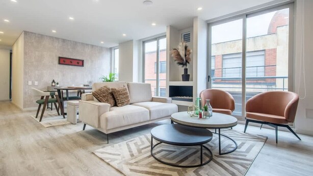A modern living room with a sofa, two armchairs, a coffee table, and a dining area with a table and chairs. - Cozy 3 Br Apartment in Usaquen (Bogotá)